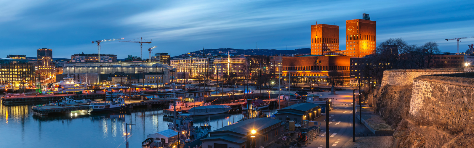 A harbor and many large buildings are filled with lights in the twilight. 